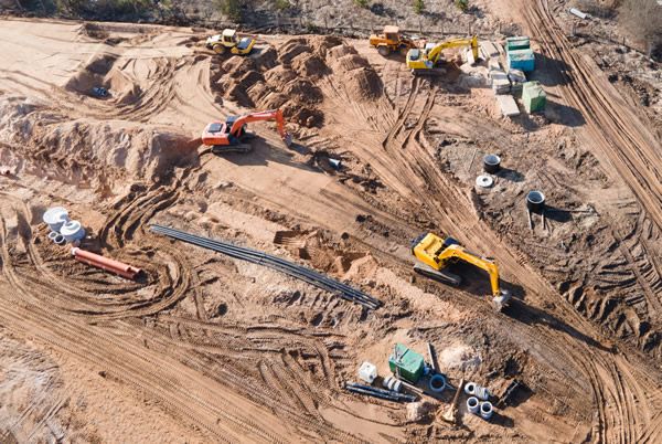 Multiple excavators and construction vehicles working on a large construction site with dirt and pipe installations